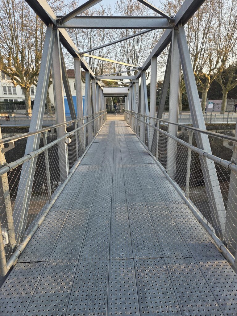 View of a modern steel pedestrian bridge with trees lining the pathway.